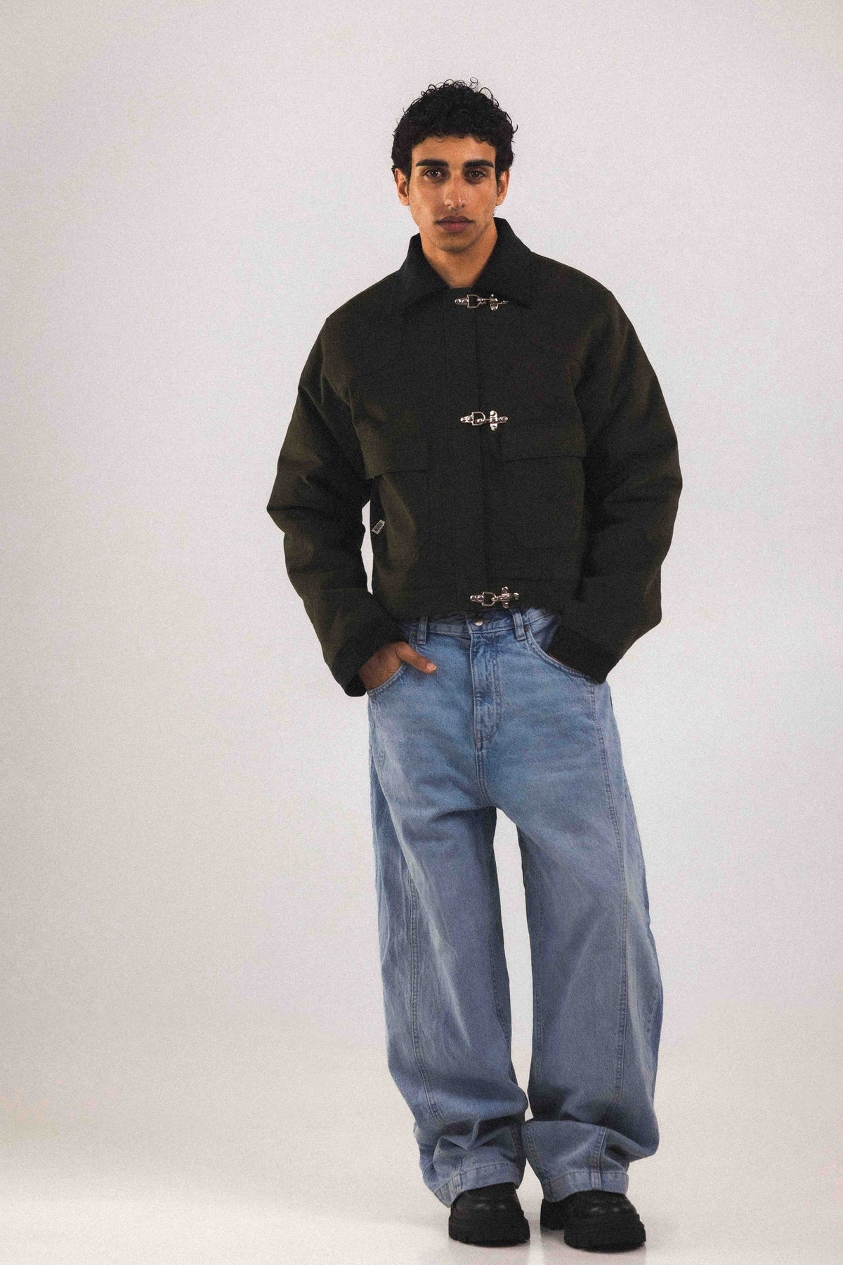 Blouson court Adam Vert, porté en mouvement, avec ses trois boucles pompiers qui se ferment au-dessus du zip, coupe unisexe pensée pour toutes les silhouettes
